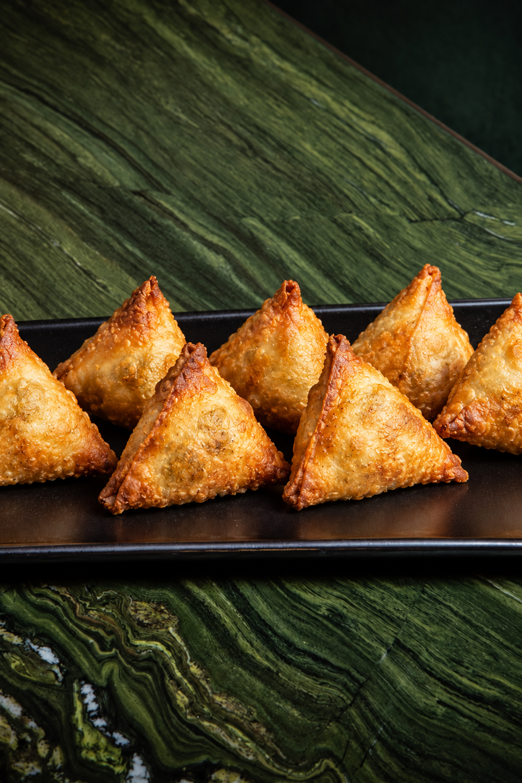 Evenly spaced golden samosas on a black serving tray